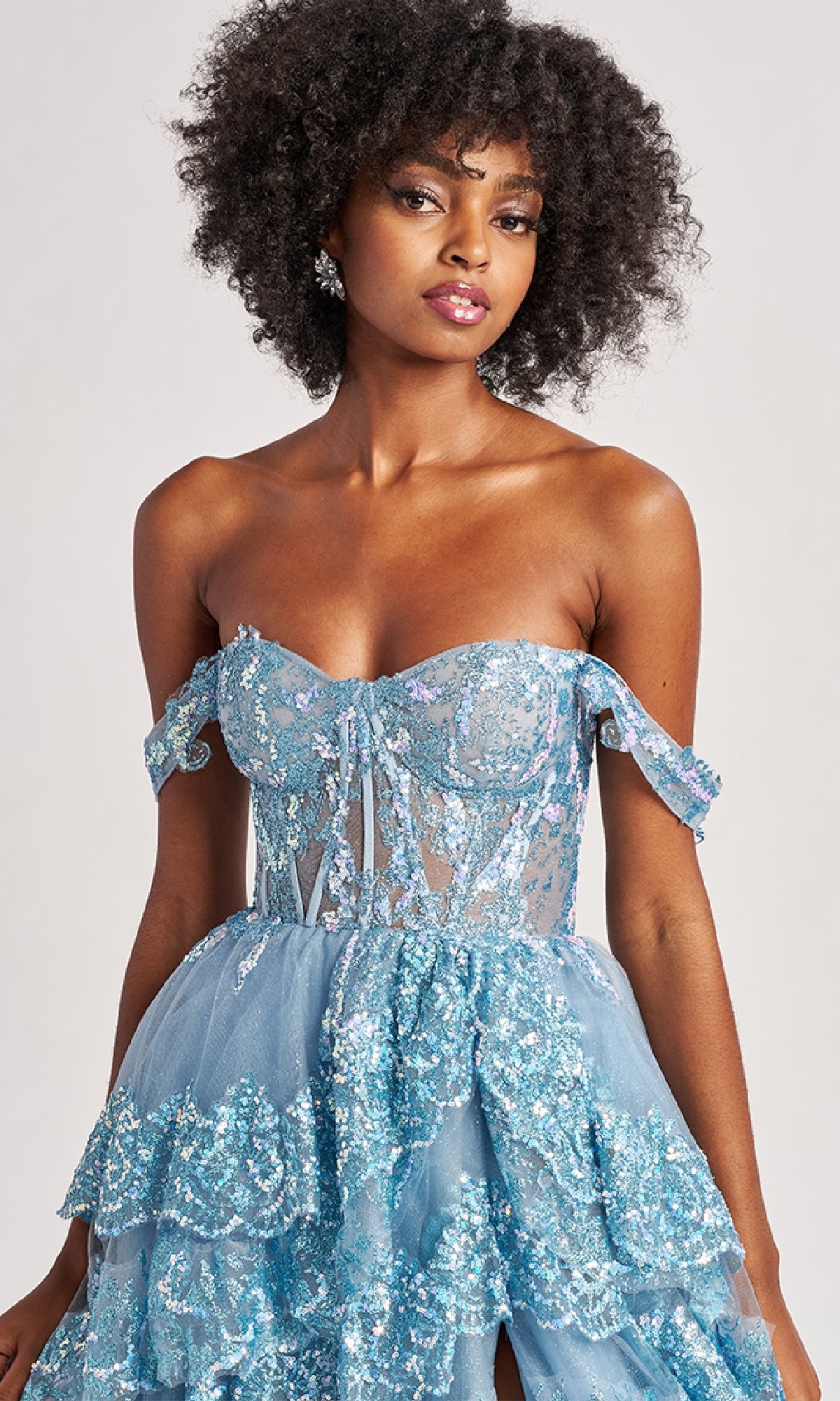 A woman models the Long Prom Dress: Colette CL8690, featuring a strapless, off-the-shoulder sequin bodice with ruffle-tiered A-line tulle skirt, standing against a plain background.